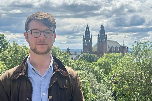 Daniel O'Malley with a green background of trees and the top of Kelvingrove Art Gallery