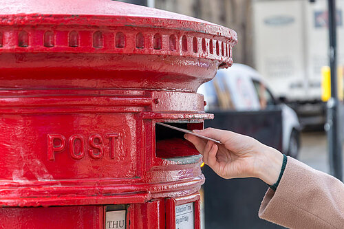 A woman posting a letter into a post box.