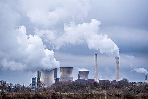 A power station with smoke blowing out of the chimneys.