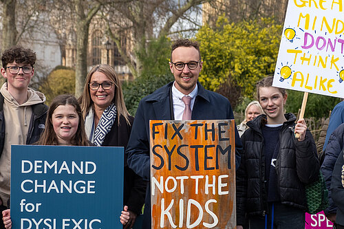 Adam Dance MP stands outside Parliament with campaigners holding signs calling for better support for dyslexic children. One sign reads “Fix the system, not the kids”.