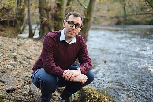 Tom Gordon MP crouching next to the River Nidd